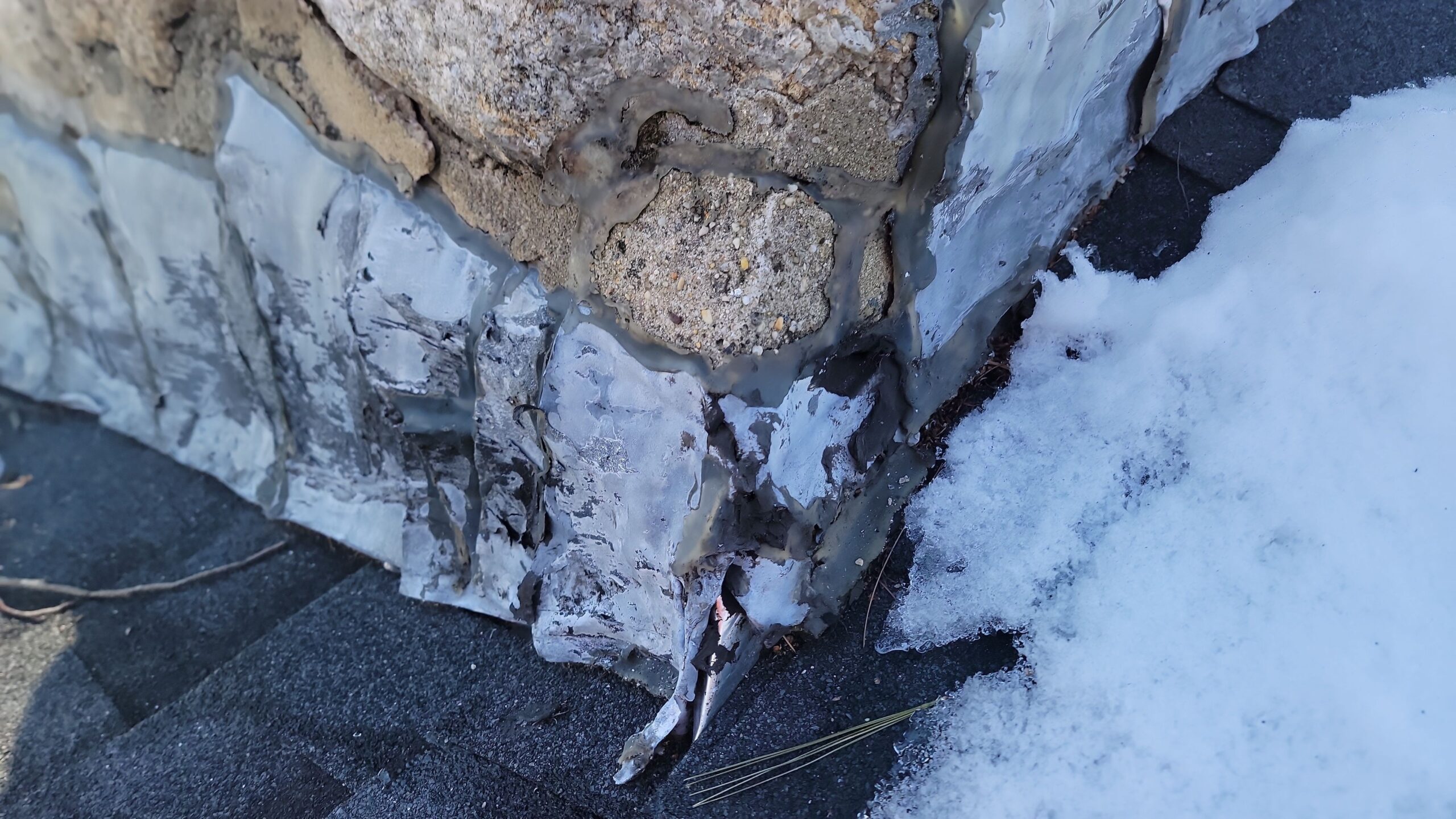 Damaged roof step flashing at chimney base with winter snow exposure in Connecticut